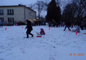 2 rodziców ciągnie na sankach swoje dzieci.