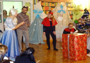 Na scenie przebrani rodzice oraz duży prezent.