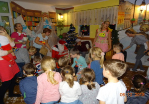 W pólkolu stoją rodzice. Swięty Mikołaj rozdaje dzieciom smakołyki.