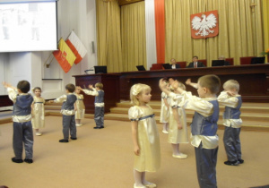Dzieci w dużej sali obrad tańczą w parach Prząśniczkę.