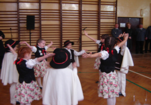 Dzieci w strojach góralskich wykonują taniec z rękoma uniesionymi do góry.