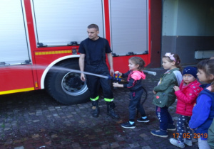 Dziewczynka leje wodę ze sprzetu strażackiego.