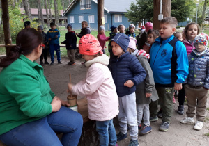 Dzieci stoją w kolejce do ubijania masła. Jedno dziecko pod nazdorem osoby dorosłej ubija masło.