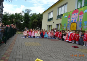 Taras przedszkolny, a na nim scenografia przedstawiająca zamek. Na tarasie stoją przedszkolaki ubrane w stroje odpowiednie do przedstawienia.