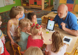 Dzieci wokół prowadzącego, który wyjaśnia zasady pracy z tabletem.