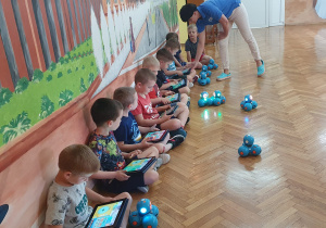 Dzieci wraz z prowadzącą za pomocą tabletów sterują swoimi robotami.