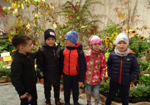 Dzieci stoją na tle jesiennych kwiatów.
