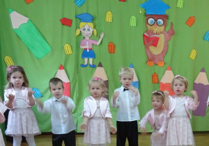 Dzieci stoją na tle dekoracji i śpiewają piosenkę.