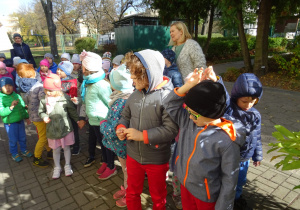 Dzieci stoją przed krzewem i przygotowują się do nasadzania roślin.