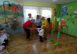 Pani Dyrektor czerwonym ołówkiem pasuje chłopca na przedszkolaka.