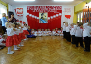 Taniec dzieci z gr. I do piosenki "O mój rozmarynie". Przedszkolaki trzymają się za głowę.Dziewczynki mają białe podkoszulki i czerwone spódniczki w groszki, chłopcy są w białych koszulach i czarnych spodniach.