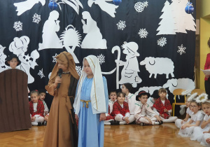 Na środku sceny stoją dzieci odgrywające rolę Maryji i Józefa.