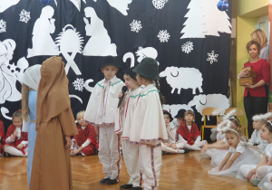 Na środku sceny stoją dzieci odgrywające rolę Józefa, Maryji i pasterzy.