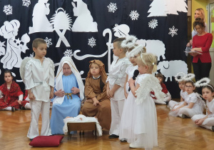 Na środku sceny siedzą dzieci odgrywające rolę Józefa, Maryji. Przy nich dzieci grające Aniołów.