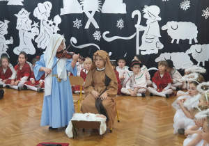 Na środku sceny dzieci odgrywające rolę Józefa, Maryji. Józef siedzi, Maryja gra na skrzypcach.