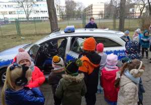 Dzieci oglądają policyjny radiowóz. Część dzieci siedzi w radiowozie.