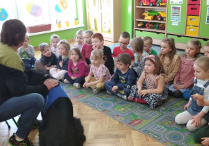 Dzieci siedzą na przeciwko terapeutki z psem.
