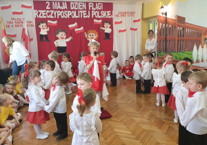 Dzieci po kole tańczą w parach, w środku dziewczynka śpiewa piosenkę.