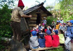 Dzieci siedzą wokół Skrzatologa. Skrzatolog pokazuje dzieciom alfabet Skrzatów.