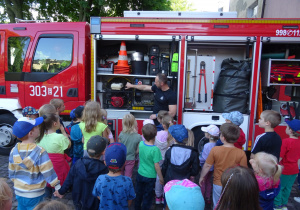 Strażak demonstruje dzieciom sprzęt znajdujący się w wozie strażackim.