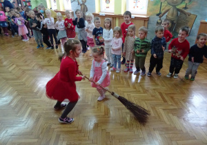 Dwie dziewczynki tańczą na środku sali z miotłą.