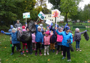 Dzieci stoją z plakatami oraz zebranymi śmieciami.