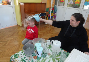 Chłopiec w czerwonej bluzce siedzi na krzesełku podczas doświadczeń z suchym lodem..