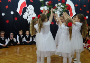 Dziewczynki w małym kółeczku trzymają róże w górze.