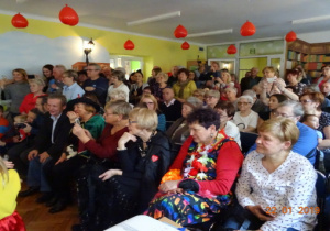 Babcie i dziakowie odladają występy wnucząt. Przy suficie wiszą czerwone balony w kształcie serc.