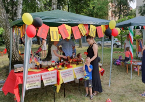 Stoiskon z potrawami kuchni niemieckiej. Przy stoisku stoją dorośli i jedno dziecko.