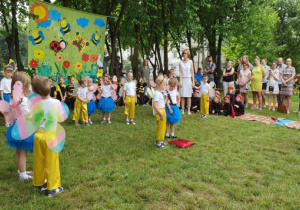 W pólkolu tańczą dzieci przebrane za motyle. W tle rodzice oglądający przedstawienie.