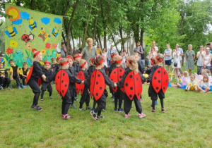 Dzieci w strojach biedronek wykonują taniec w kole.