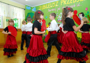 Na tle dekoracji z tortem i bajkowymi postaciami chłopcy i dziewczęta z wachlarzami wykonują taniec Flamenco.