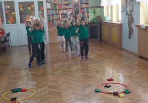 Przedszkolaki podczas zabaw sportowych z obręczami i woreczkami.